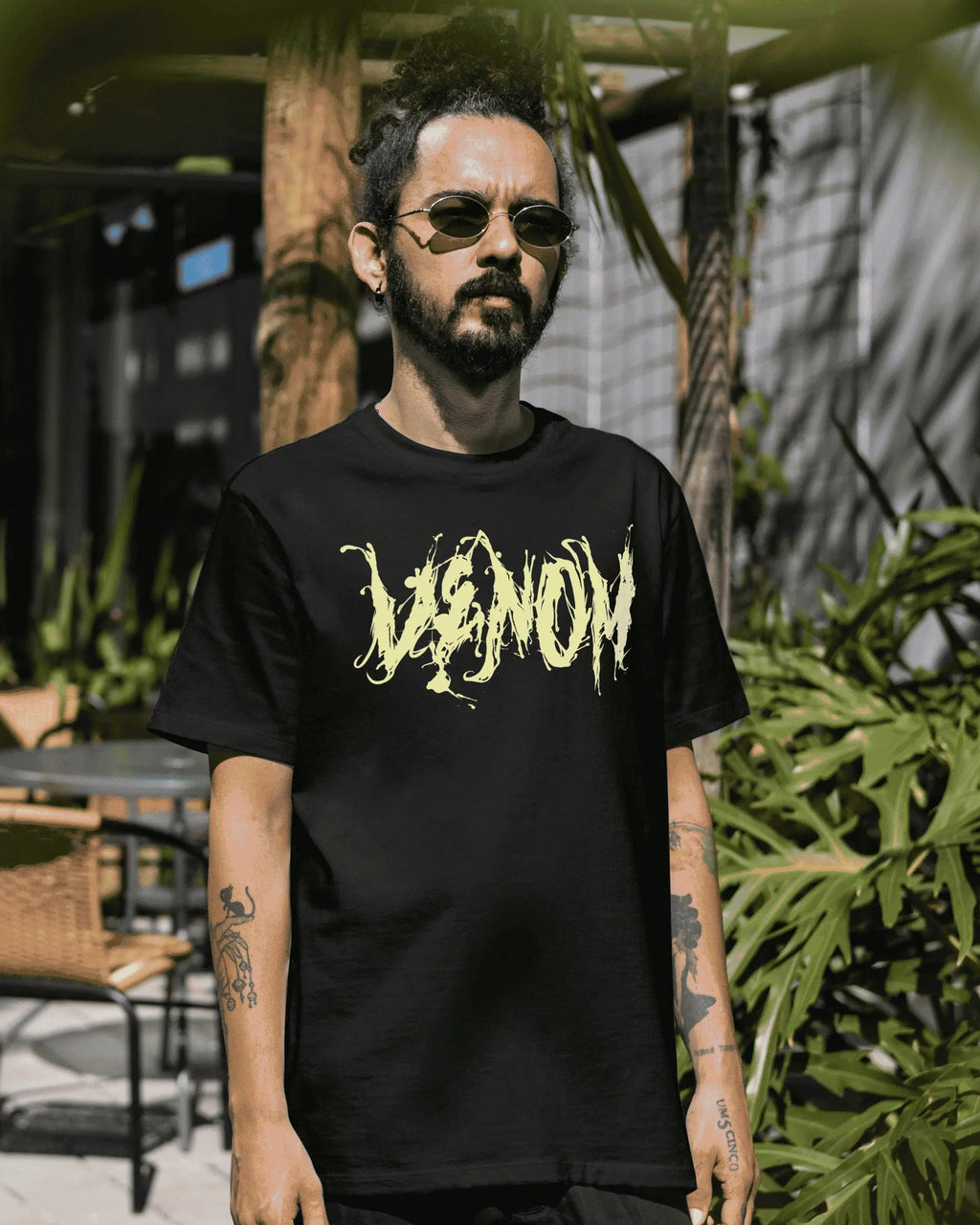 Man wearing a black t-shirt with yellow text standing outdoors among greenery